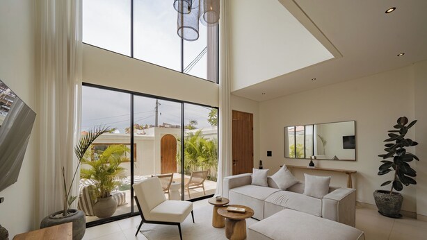 A modern living room with a large sofa, a coffee table, and a chair. There is a large window with a view of the outside. - Villa JB Canggu (Canggu)
