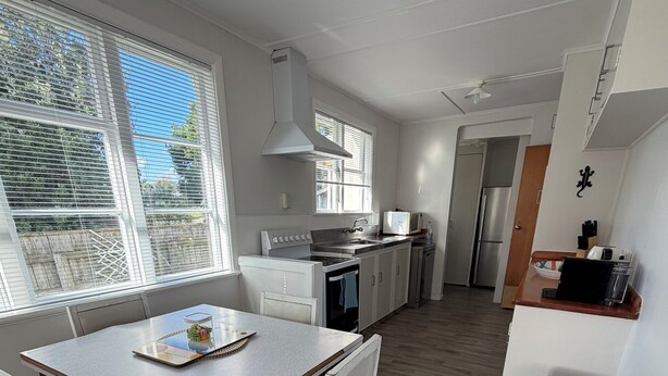 A modern kitchen with white cabinetry, a stainless steel refrigerator, and a dining area with a wooden table and white chairs. - Kowhai on Douglas – Your Relaxing Escape (Levin)