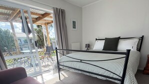A bedroom with a bed, a sofa, a sliding glass door to a patio, and a small table with a lamp. - Kowhai on Douglas – Your Relaxing Escape (Levin)