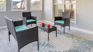 Una habitación con cuatro sillas de mimbre con cojines azul turquesa, una mesita de centro y un ventanal con persianas.