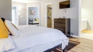 Un dormitorio con cama, ventilador de techo, televisor, cómoda y vestidor.