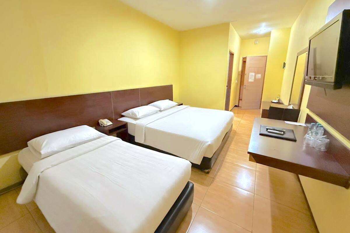 Une chambre d’hôtel avec deux lits, un bureau doté d’un téléphone et d’une télécommande, et un téléviseur.