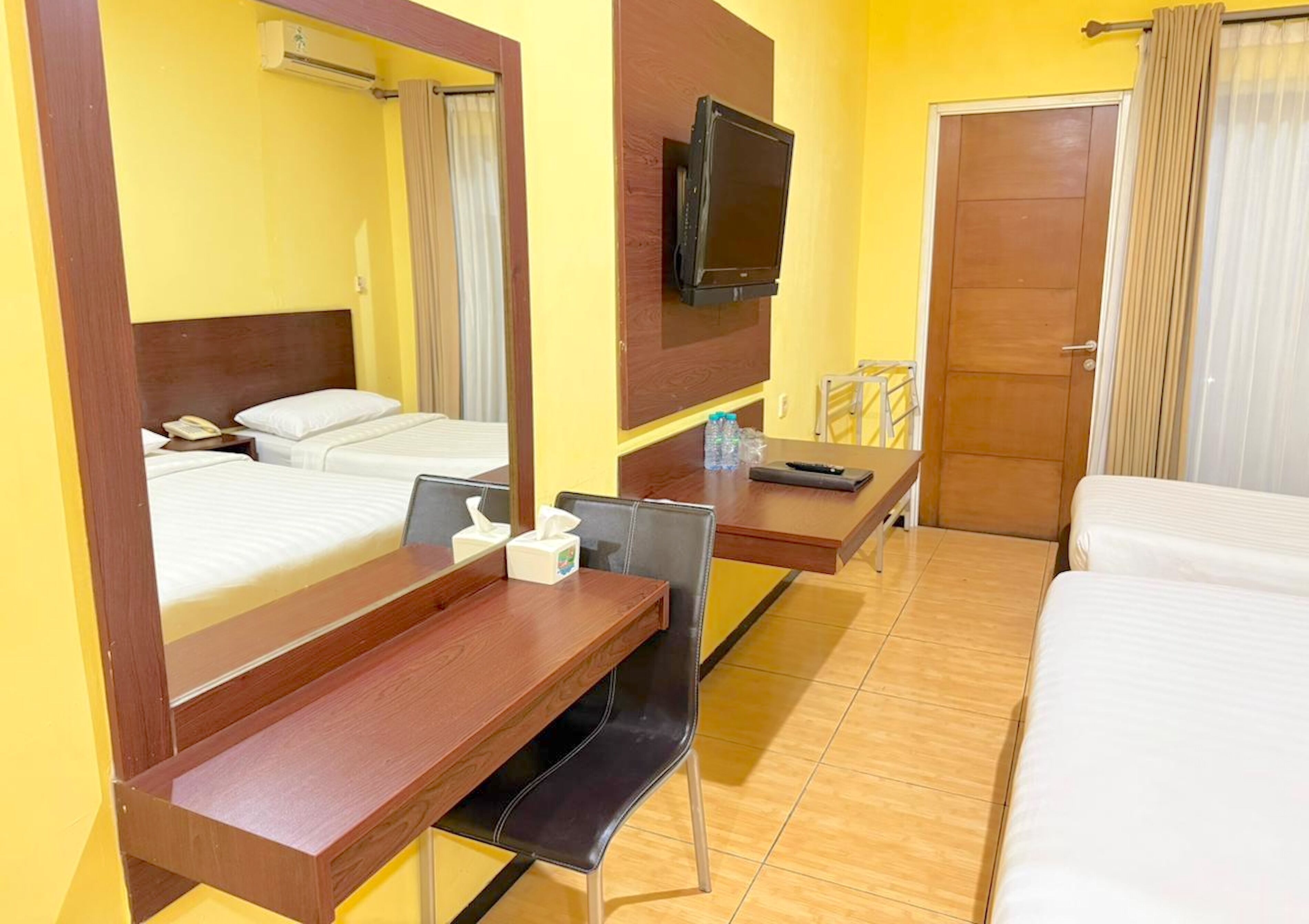 A hotel room with two beds, a desk with a chair, a television mounted on the wall, and a door.