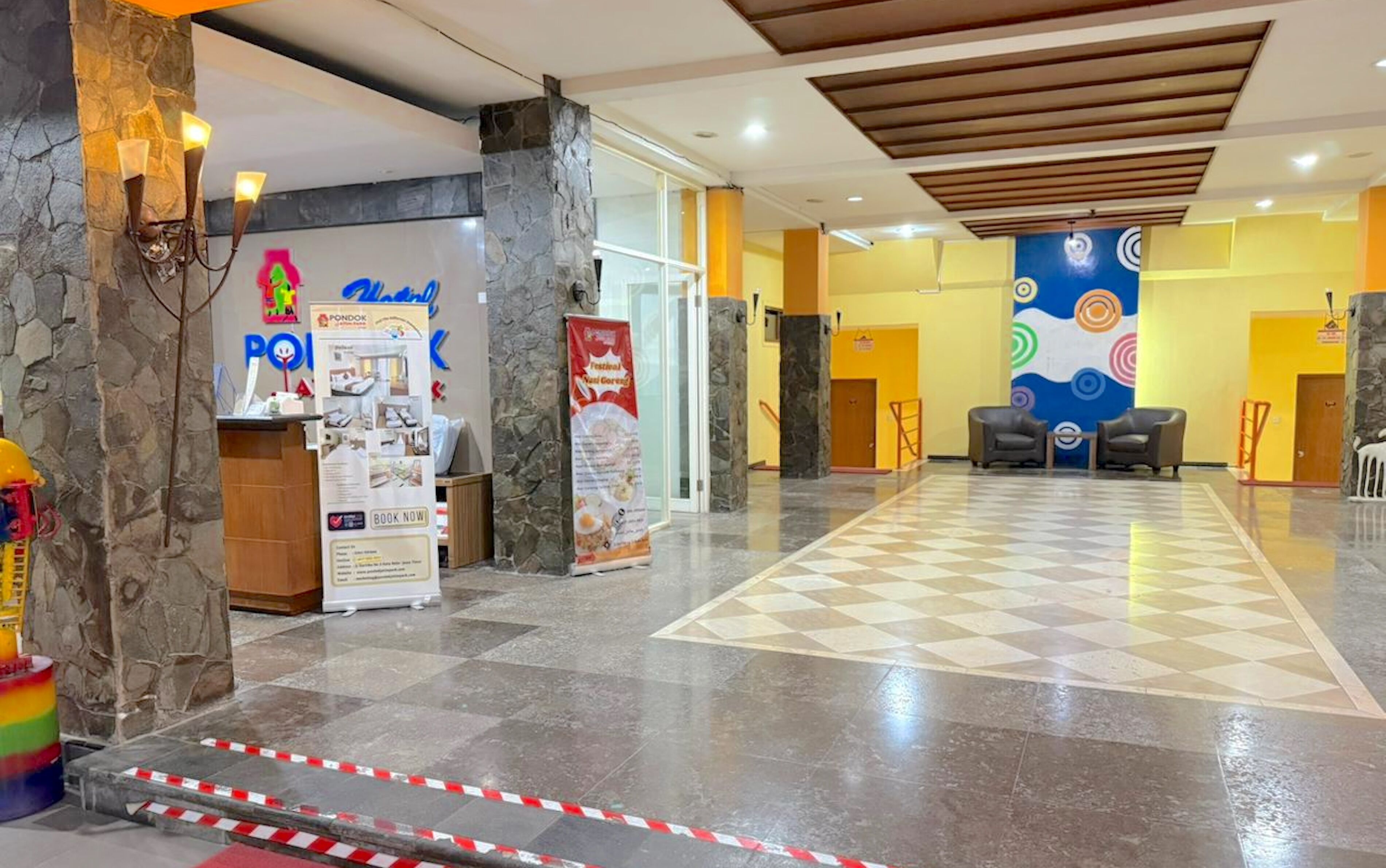 A hotel lobby with a checkered floor, stone pillars, and a colorful wall mural.