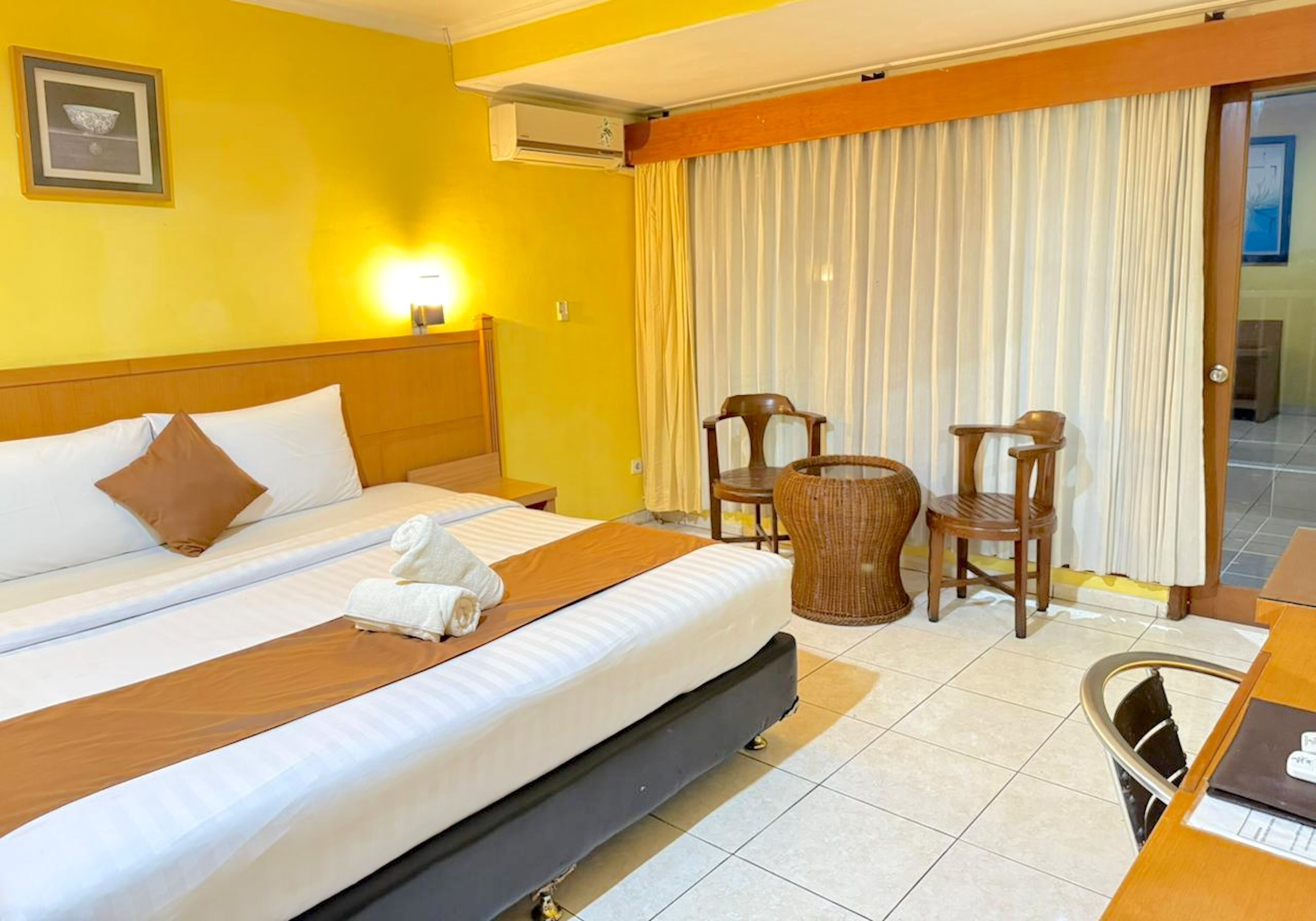 A hotel room with a large bed, a desk with a chair, a small round table, and a window with curtains.