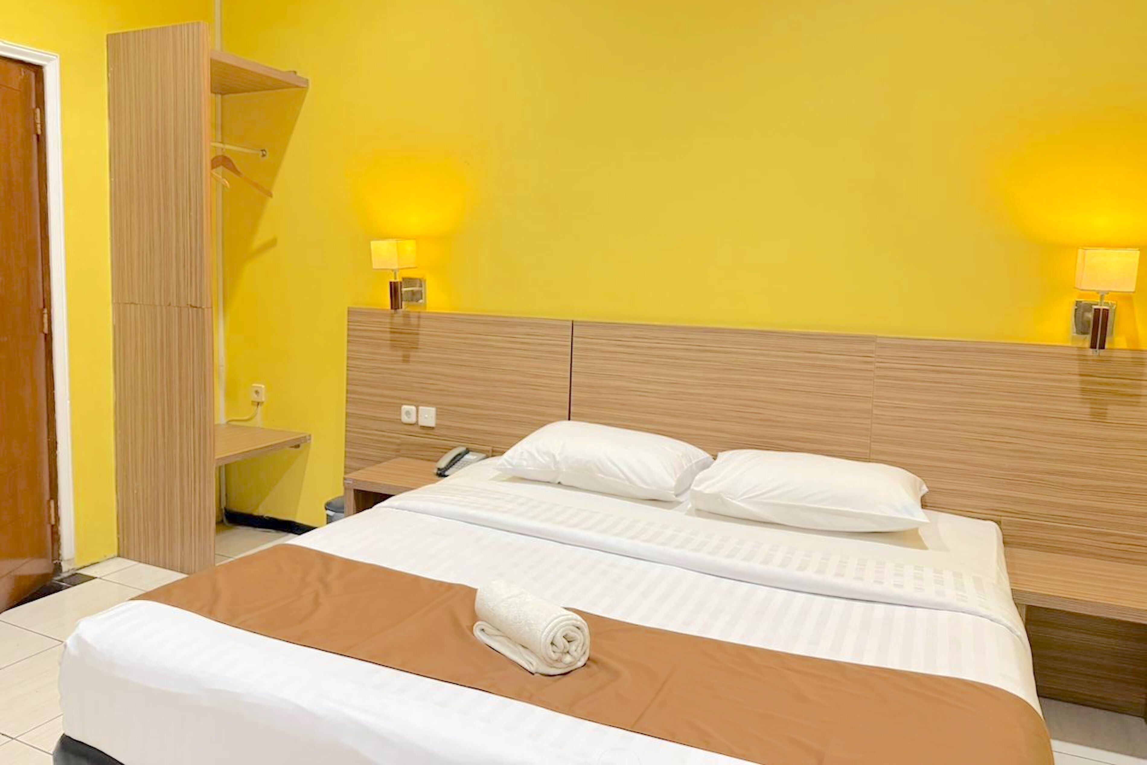 A hotel room with a bed, two bedside lamps, a wooden headboard, and a brown accent on the bed.