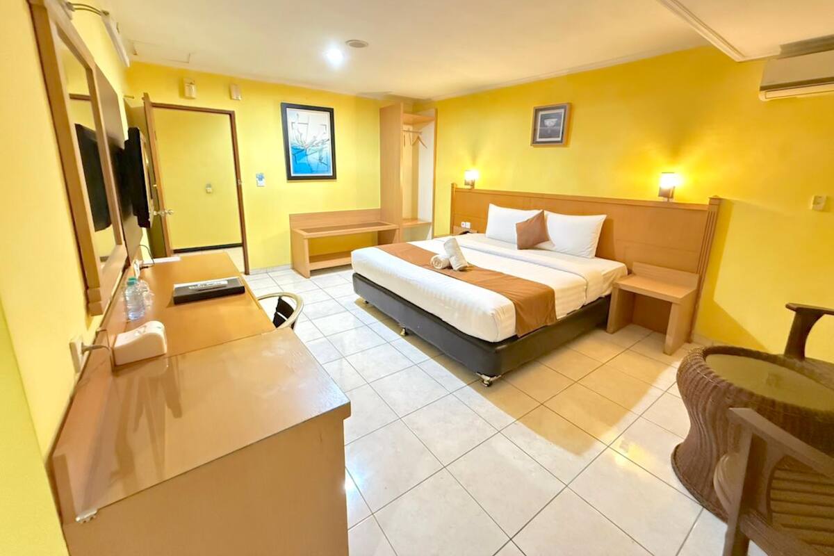 Une chambre d’hôtel avec un lit, des tables de chevet, un bureau et un miroir.