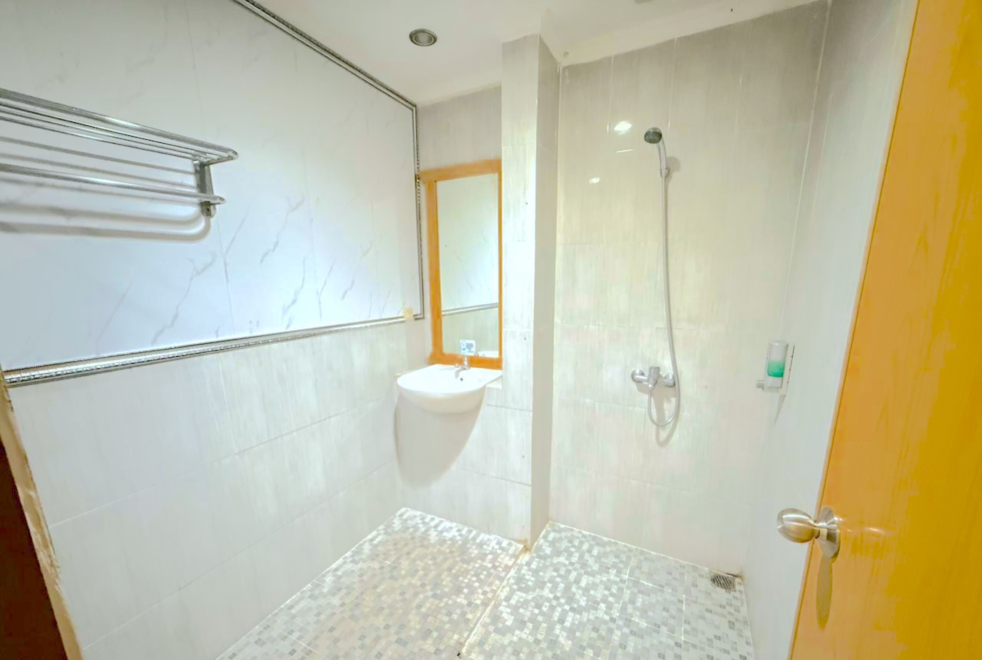 Un baño con lavamanos blanco, espejo, ducha y piso de baldosas.