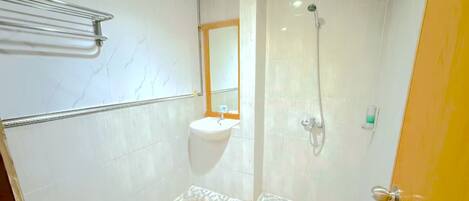 Un baño con lavamanos blanco, espejo, ducha y piso de baldosas.