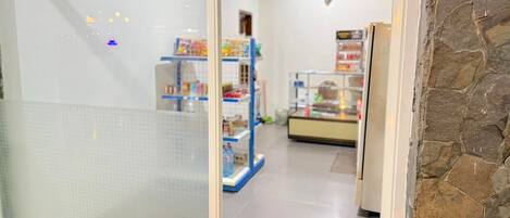Um corredor com parede revestida de azulejos, parede de pedra à direita e prateleiras com diversos objetos ao fundo.