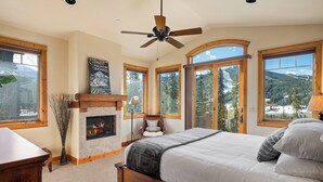 A bedroom with a fireplace, large windows, and a bed. - Lakota Dreamcatcher North | Sauna | Slope Views | Private Hot Tub (Winter Park)