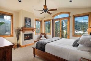 A bedroom with a fireplace, large windows, and a bed. - Lakota Dreamcatcher North | Sauna | Slope Views | Private Hot Tub (Winter Park)