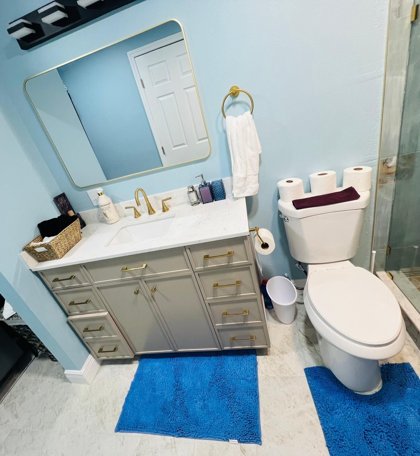 Et badeværelse med en hvid vask, guldarmatur, et hvidt toilet og en blå måtte.
