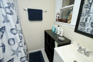 A bathroom with a white sink, a black vanity, a blue towel, and a window with a view of pinecones and a stuffed animal.