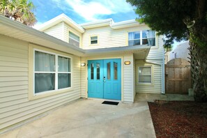 A two-story house with a blue front door, a small porch, and a wooden fence.