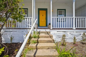 Une maison avec une porte jaune, des balustrades blanches et un escalier en pierre menant au porche d’entrée.