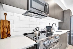 A modern kitchen with a stainless steel range hood, a built-in microwave, and a gas stove. - Bay View Studio | Rooftop Pool, Downtown Miami (Miami)