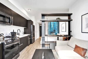 A modern kitchen with dark cabinetry, stainless steel appliances, and a view of a cityscape through a large window. - Bay View Studio | Rooftop Pool, Downtown Miami (Miami)
