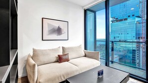 A modern living room with a sofa, a coffee table, a framed picture, and a large window offering a city view. - Bay View Studio | Rooftop Pool, Downtown Miami (Miami)