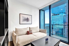 A modern living room with a sofa, a coffee table, a framed picture, and a large window offering a city view. - Bay View Studio | Rooftop Pool, Downtown Miami (Miami)