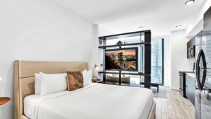 A modern hotel room with a large bed, a flat-screen TV, a refrigerator, and a view of a cityscape. - Bay View Studio | Rooftop Pool, Downtown Miami (Miami)