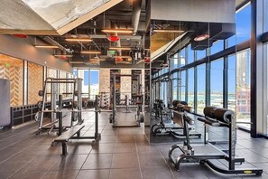 A gym with various weightlifting equipment, large windows, and a view of the city. - Bay View Studio | Rooftop Pool, Downtown Miami (Miami)