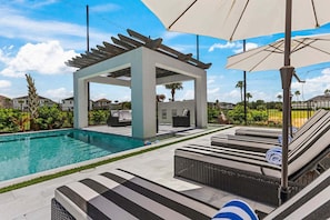 Un área de piscina con sillones, una pérgola y sombrillas.