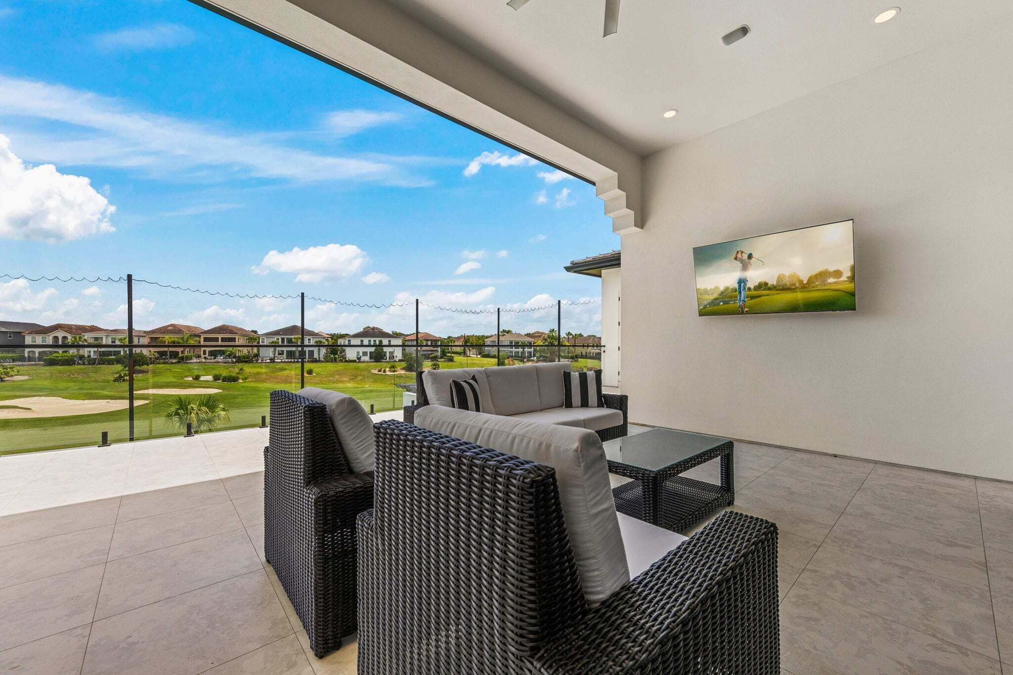 Une terrasse extérieure moderne, aménagée avec des meubles en osier, un téléviseur à écran plat et offrant une vue sur un terrain de golf.