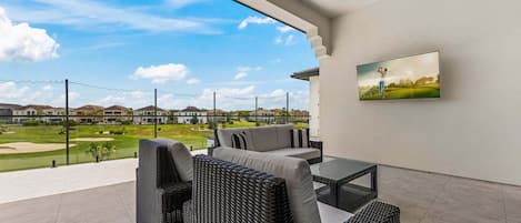 A modern outdoor patio with wicker furniture, a flat-screen TV, and a view of a golf course.