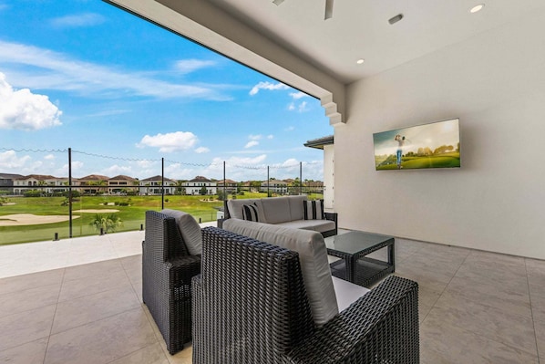 Un patio exterior moderno con mobiliario de mimbre, un televisor de pantalla plana y vistas a un campo de golf.