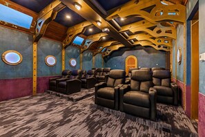Un salón de cine en casa con varios sillones reclinables, piso alfombrado y techo de madera con aberturas circulares.