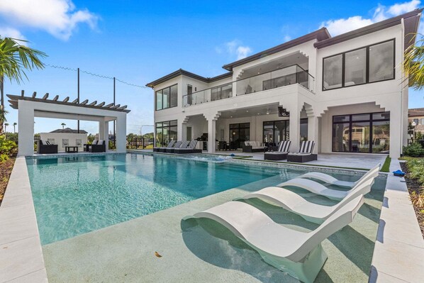 Una casa moderna de dos pisos con piscina, mobiliario exterior y un pérgola.