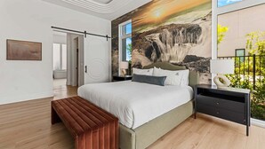 Quarto com uma cama grande, um banquinho, uma mesa de cabeceira e um mural na parede com uma cascata.
