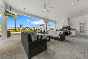 Un amplio espacio al aire libre con ventilador de techo, televisor, piscina y zona de cocina.