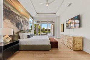 A modern bedroom with a large bed, a nightstand, a wall-mounted TV, and a view of an outdoor swimming pool. - The Nautilus at Reunion-TT488 (Kissimmee)