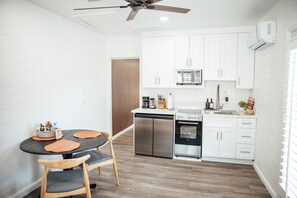 A compact kitchen with white cabinets, a built-in microwave, a stainless steel refrigerator, and an oven. There is a dining table with two chairs and a ceiling fan above. - Scottsdale Comfort: Renovated Apartment with Sunny Patio - Walkable to Old Town! (Scottsdale)