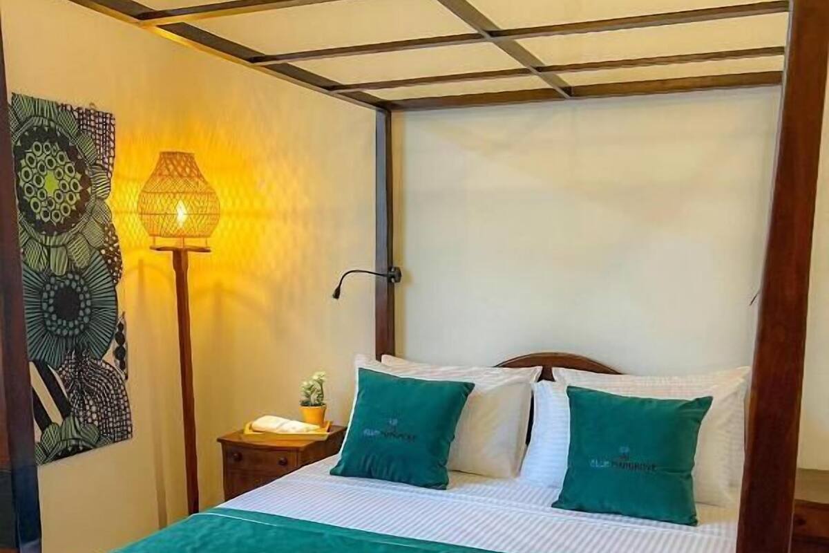 Una cama con dosel de madera, ropa de cama blanca y almohadones verdes.
