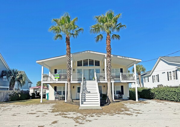 Ein zweistöckiges Strandhaus mit Balkon, Palmen und blauem Himmel.