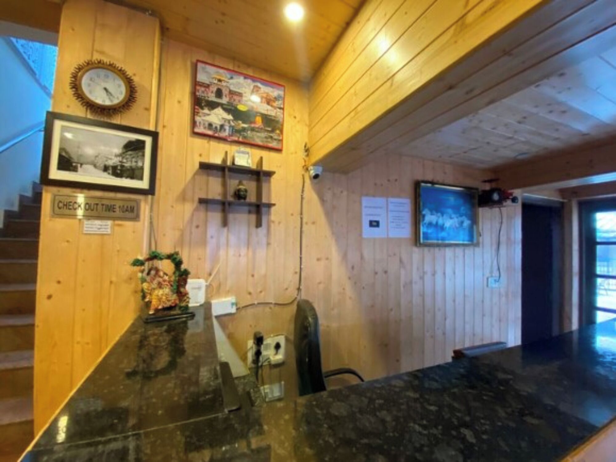 A reception desk with a clock, framed photos, a check-out sign, and a poster on the wall.