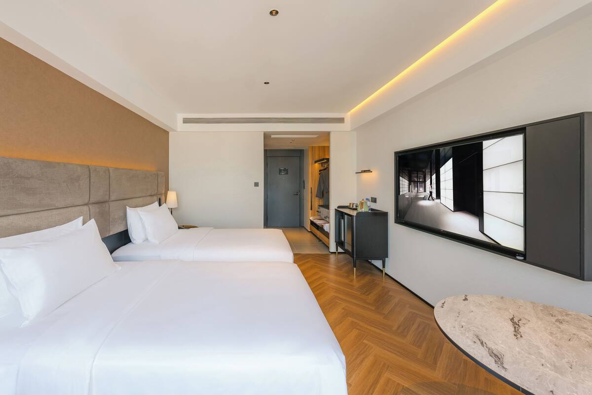 Ein Hotelzimmer mit zwei Betten, einem großen Spiegel und Holzboden.
