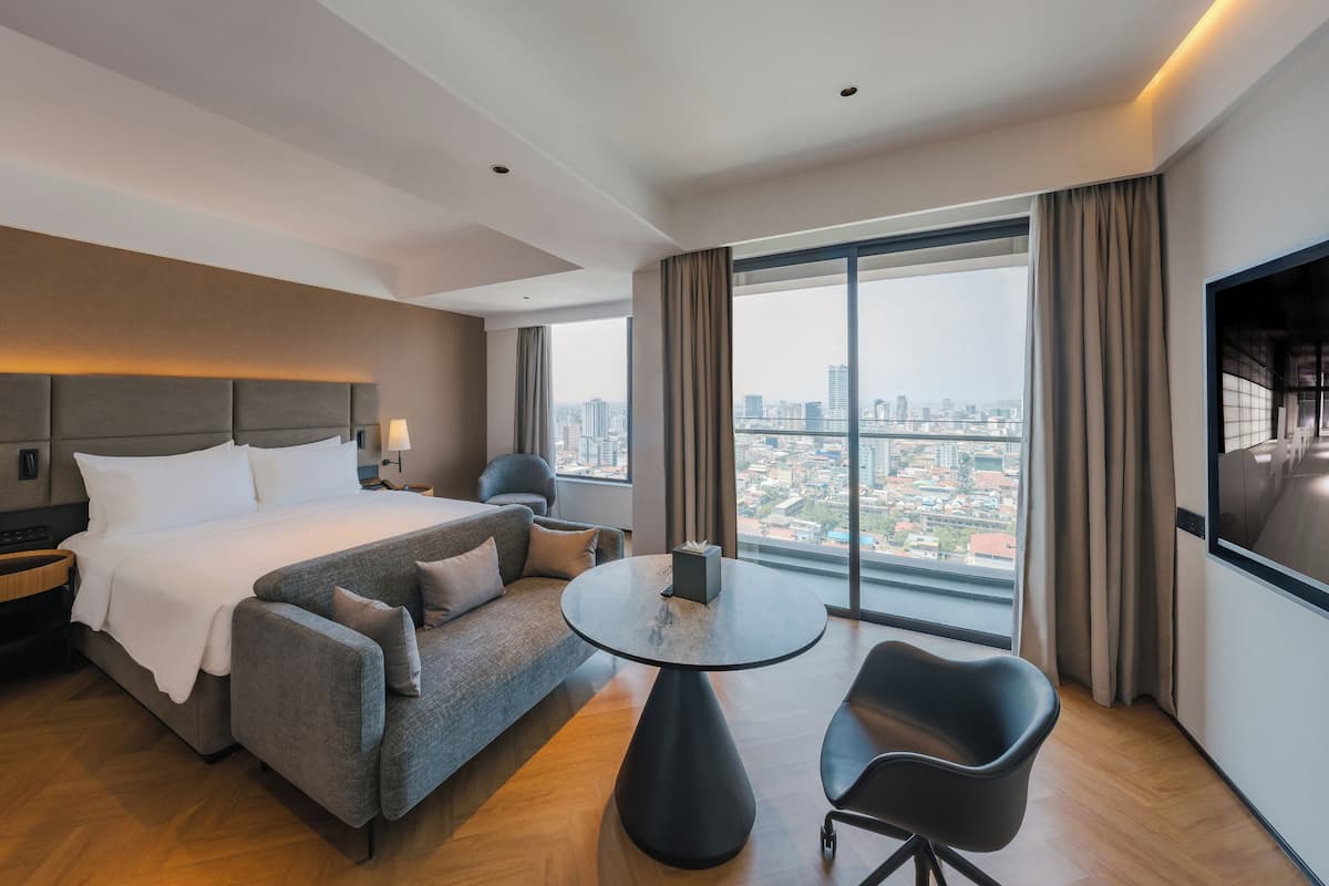 Ein modernes Hotelzimmer mit einem großen Bett, einer Couch, einem runden Tisch und Blick auf die Stadt.