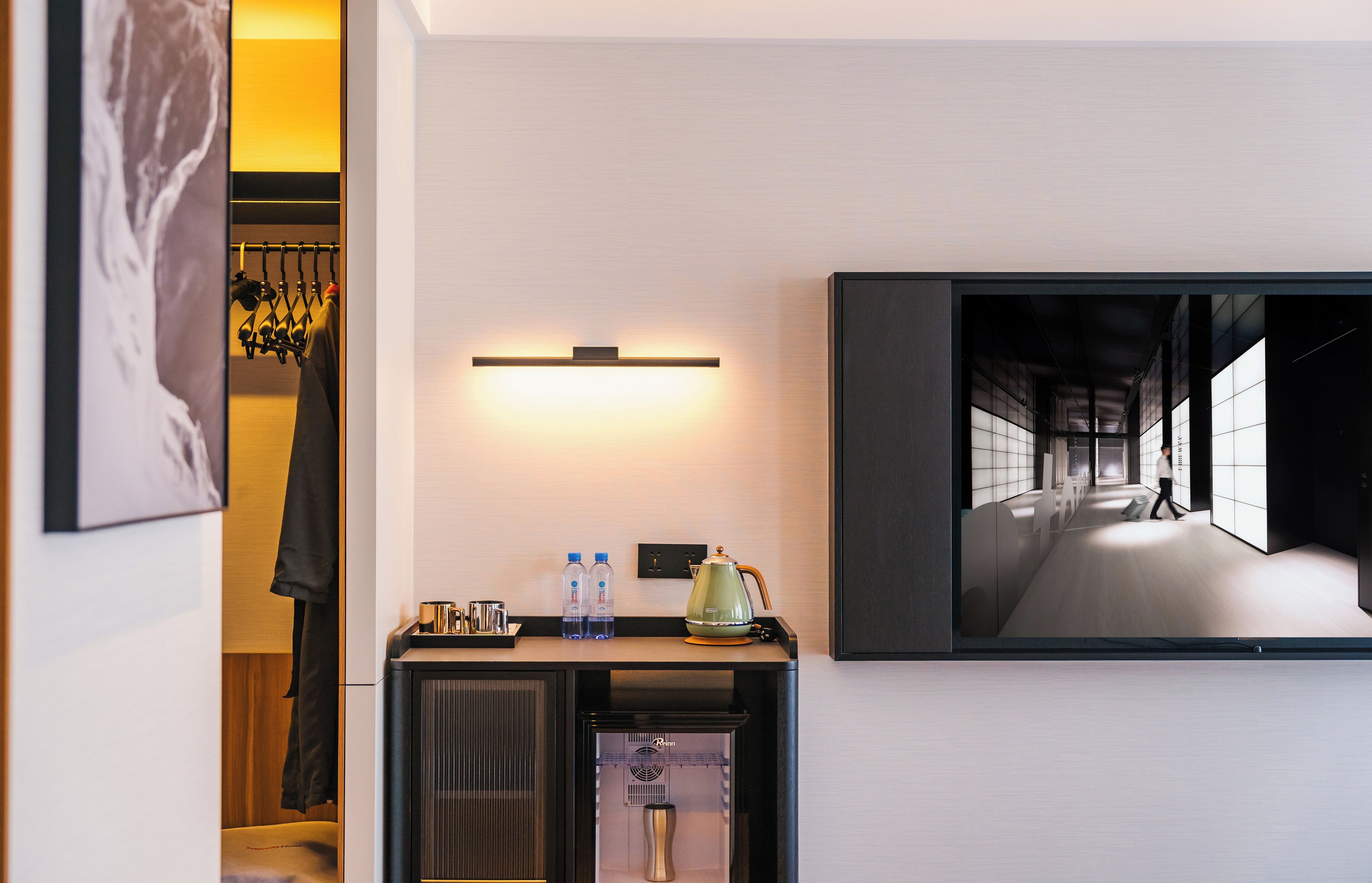 Une chambre d’hôtel équipée d’un mini-bar, d’un téléviseur à écran plat fixé au mur et d’un tableau représentant un couloir.