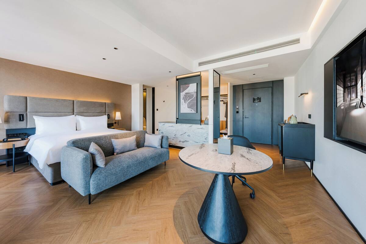 Ein modernes Hotelzimmer mit einem Bett, einer Couch, einem runden Tisch und einem Schreibtisch.