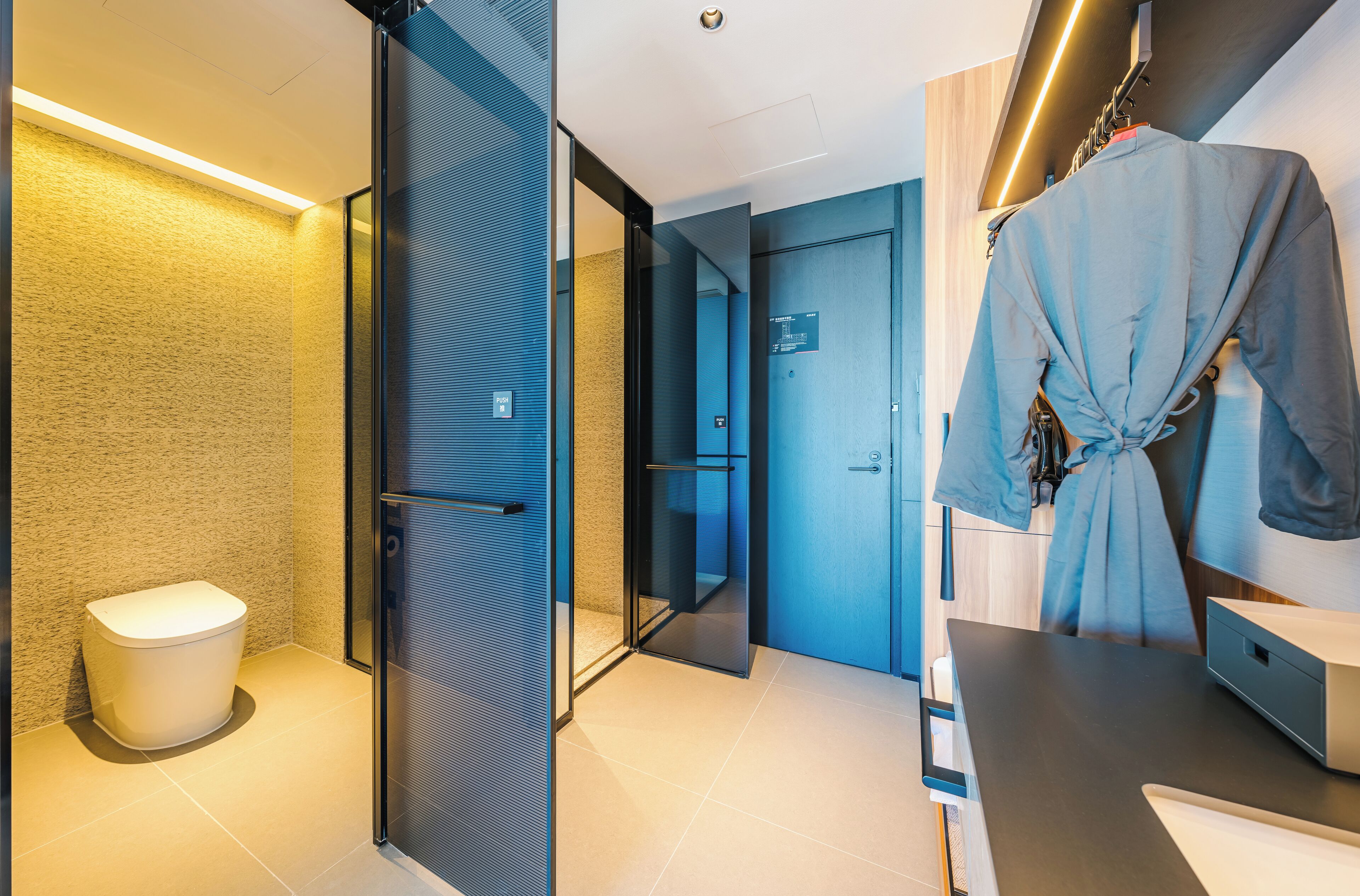 A modern bathroom with a glass partition, a white toilet, and a robe hanging on a rack.