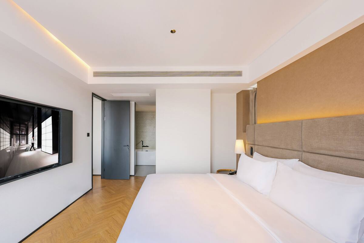 Ein modernes Hotelzimmer mit einem großen Bett, einem Flachbildfernseher und einem durchgegangene Tür erreichbaren Badezimmer.