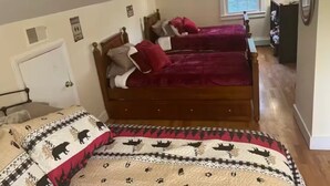 A bedroom with two wooden beds, each with a red blanket and pillows. There is a window with a view of trees, a door, and a dresser with a mirror. - Delightful 4-bedroom house in Windham. 1 mile to Windham resort & walk to town. (Windham)