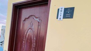 En dörr av trä med detaljerade sniderier, ett handtag av metall och en skylt ovanför som visar ”LÄGENHET 6” och ”NÄSTA LÄGENHETER”, tillsammans med en logotyp.