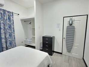 Un dormitorio con cama, armario, prenda colgada y cesto de ropa.