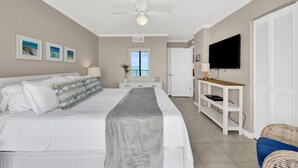 Quarto com cama, ventoinha no teto, TV e janela com vista.