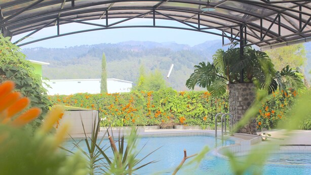 A pool area with a view of mountains, surrounded by lush greenery and orange flowers. - De View Hotel Batu (Batu)